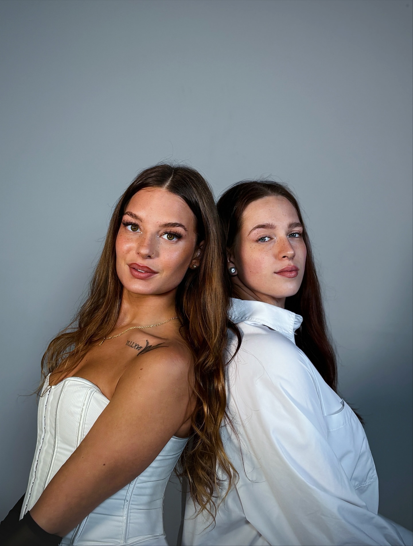 Zwei Models in Weiß Rücken an Rücken vor hellem Hintergrund
