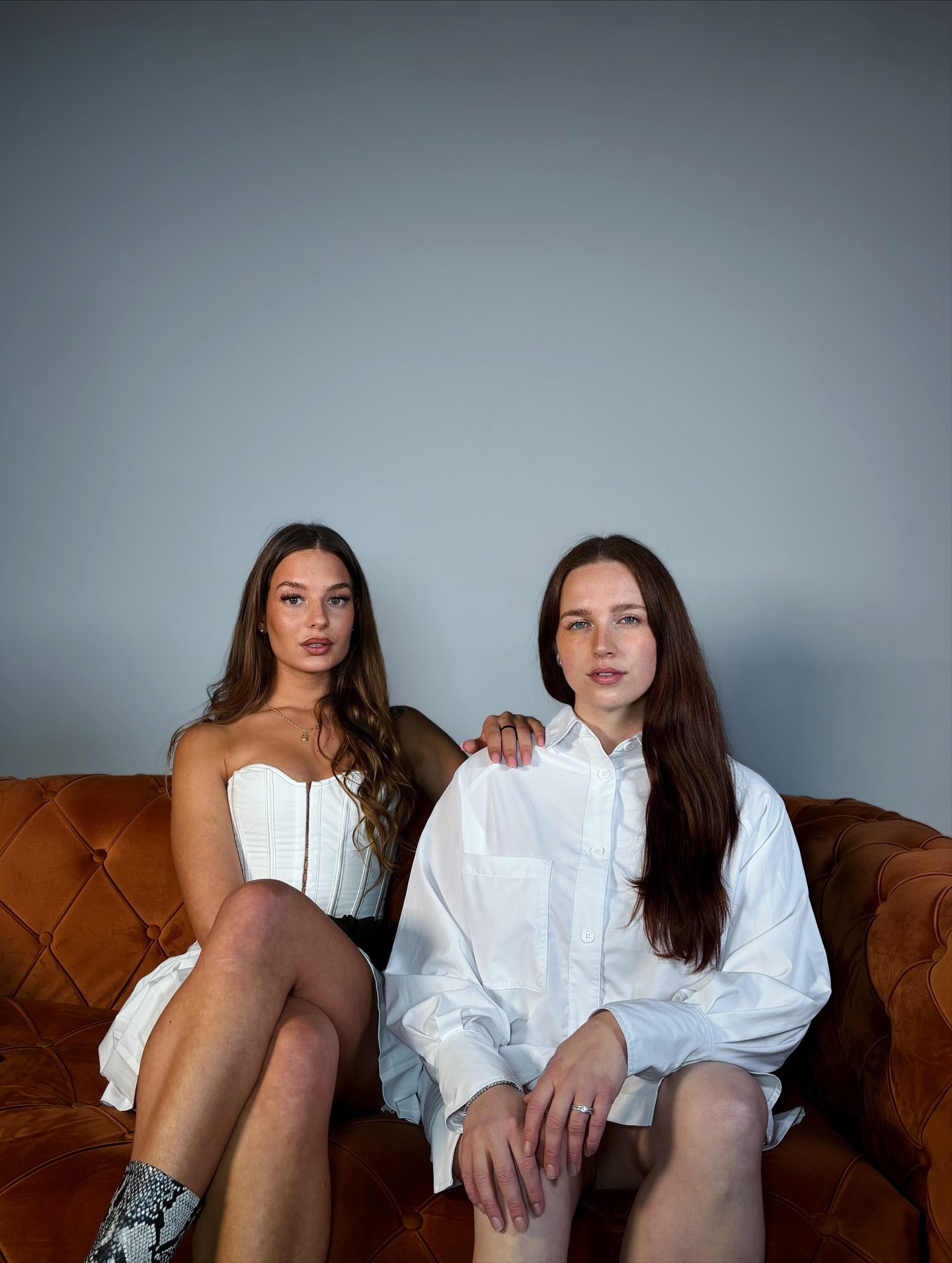 Fashion-Editorial: zwei Models in Weiß auf einem orangefarbenen Samtsofa