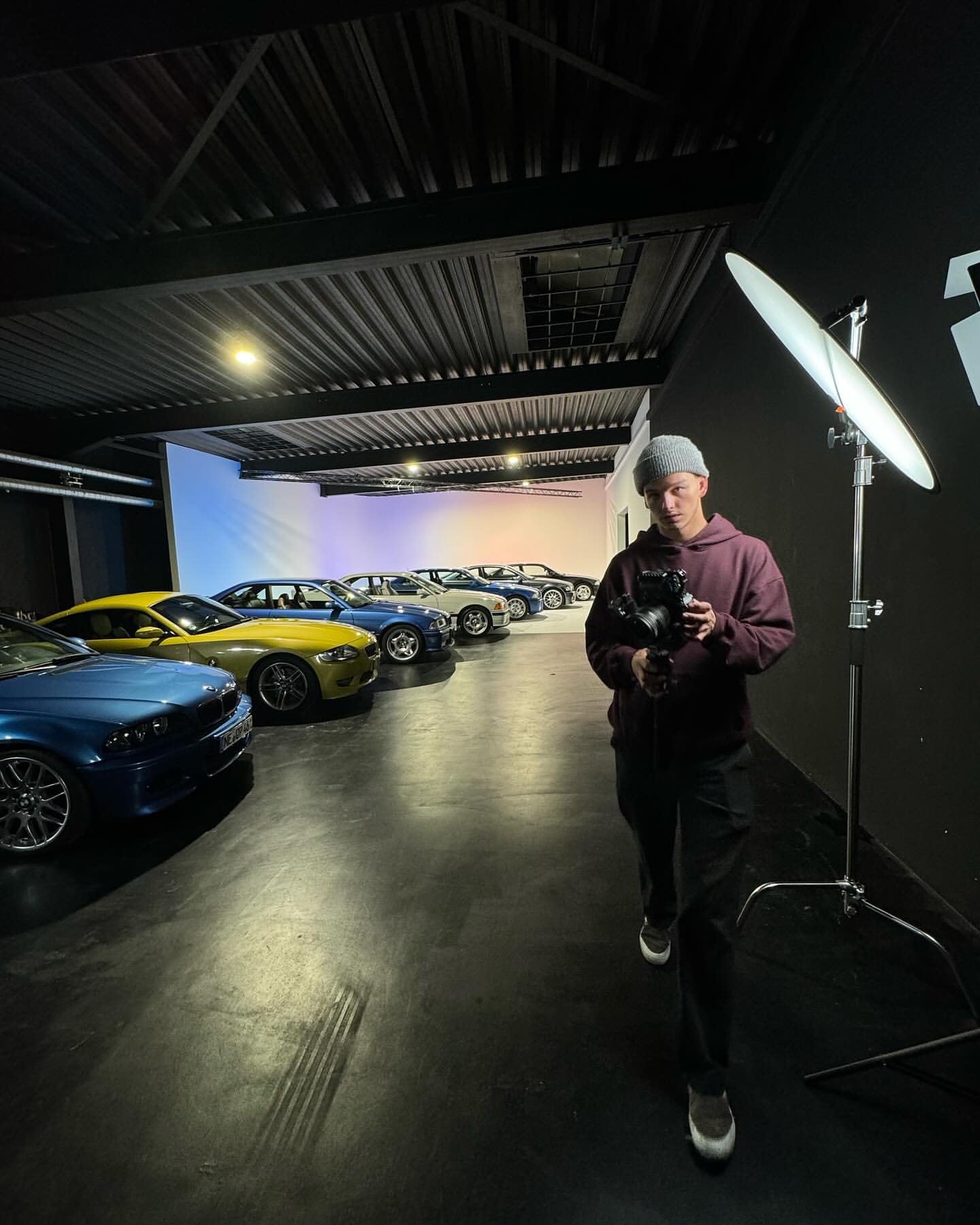 Fotograf mit Kamera vor einer Reihe Sportwagen in blau-magenta Neonlicht
